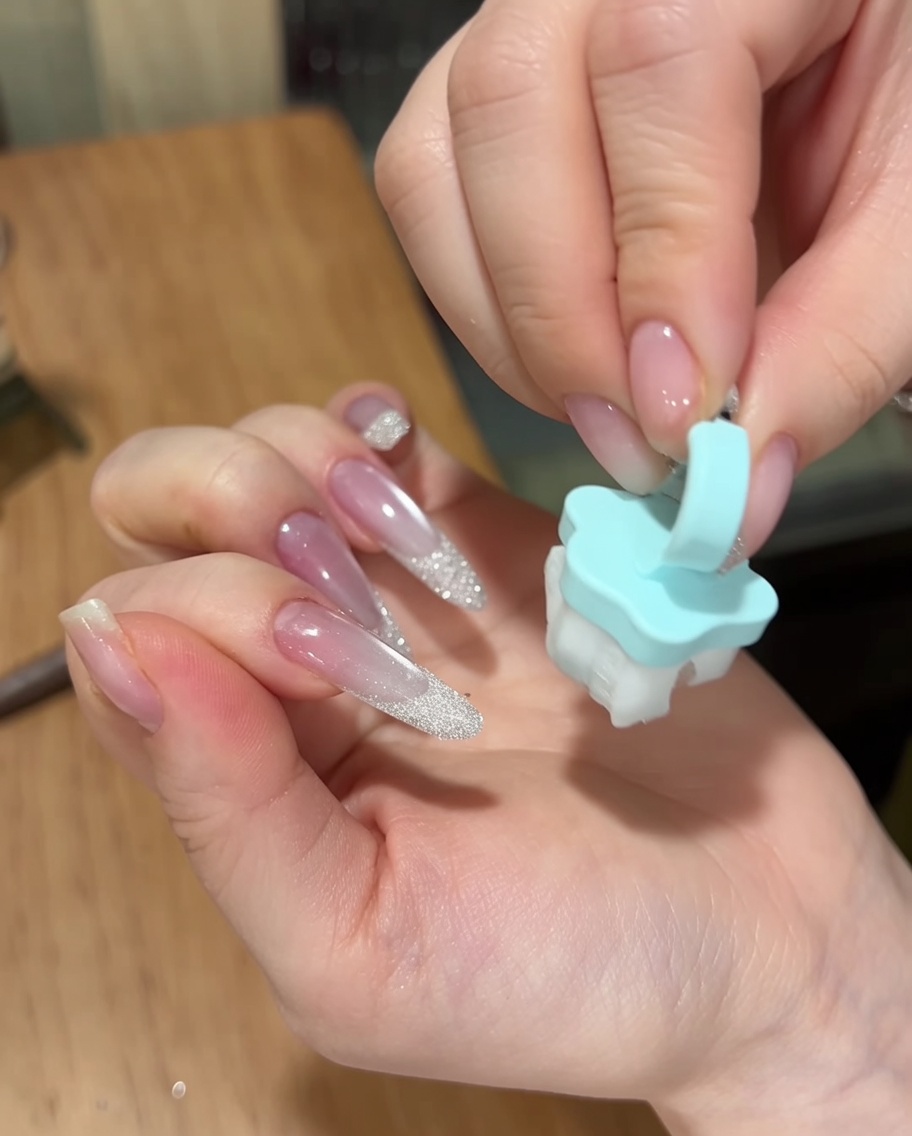 A hand using a small, soft blue brush to dust excess sugar powder off the surface of a finished manicure.