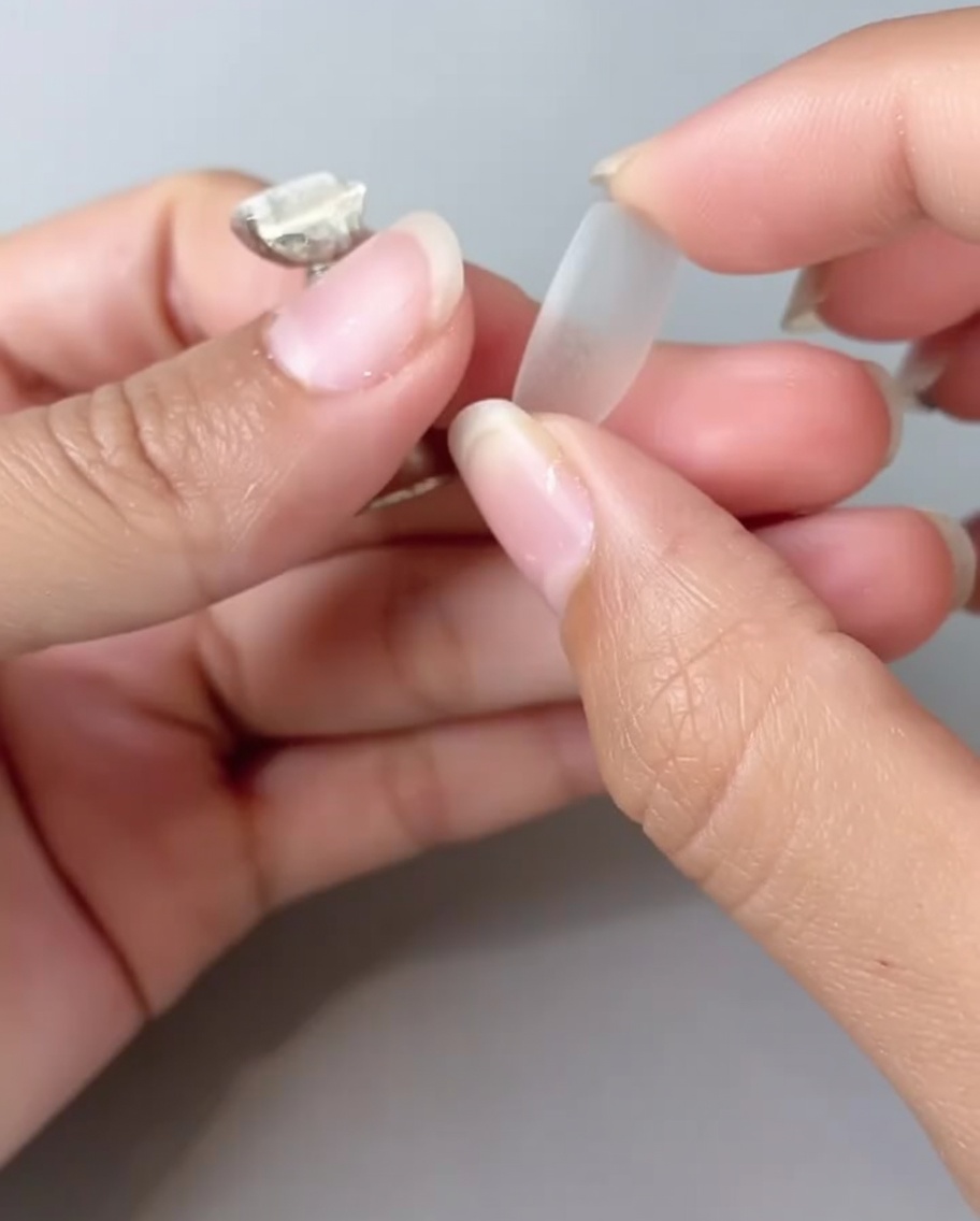 A close-up view of a persons fingers holding a clear nail tip, flipping it to show the reverse side.