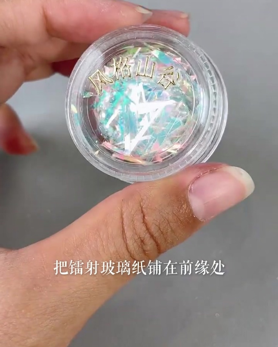 Tiny pieces of iridescent laser glass paper being placed onto the edge of a nail tip using a precision tool.