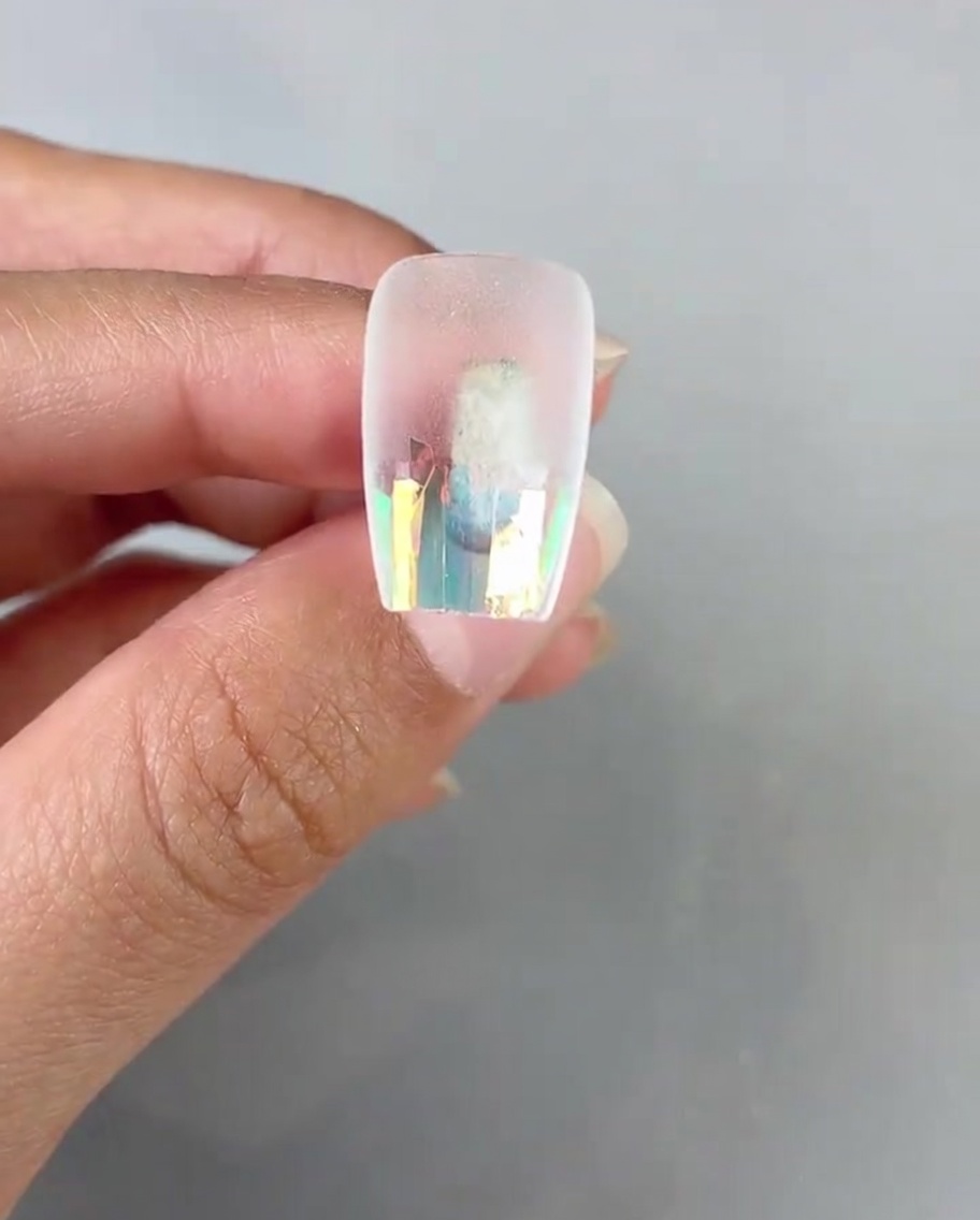 A nail brush applying a coat of clear top gel over the laser glass paper on the nail tip.