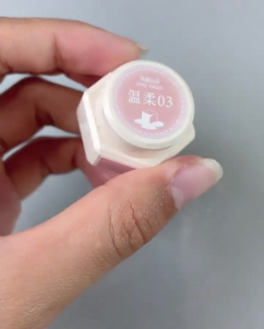 A brush applying a layer of pink gel polish to the base area of a nail tip.