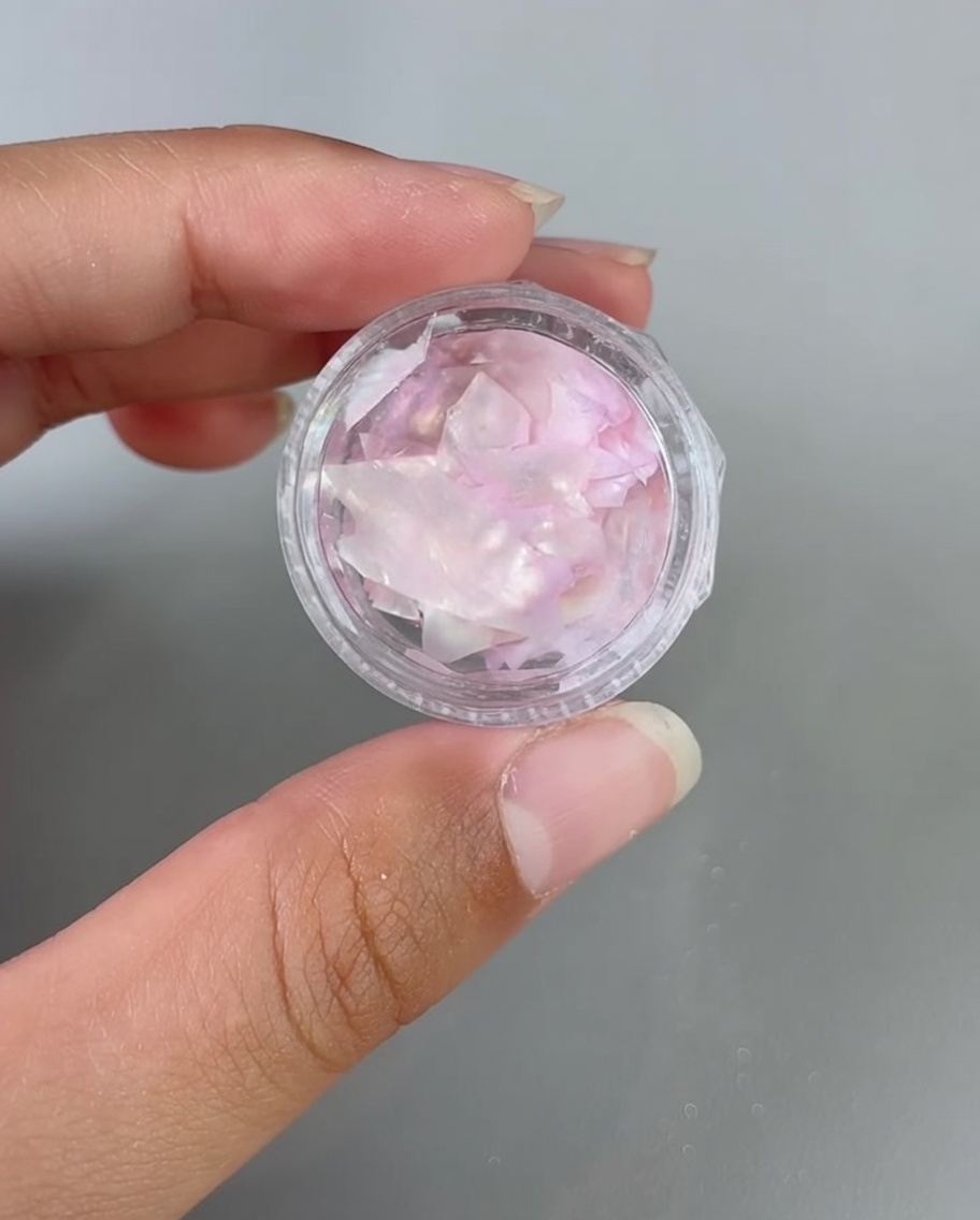 Tweezers placing iridescent shell fragments onto a gel-coated nail.