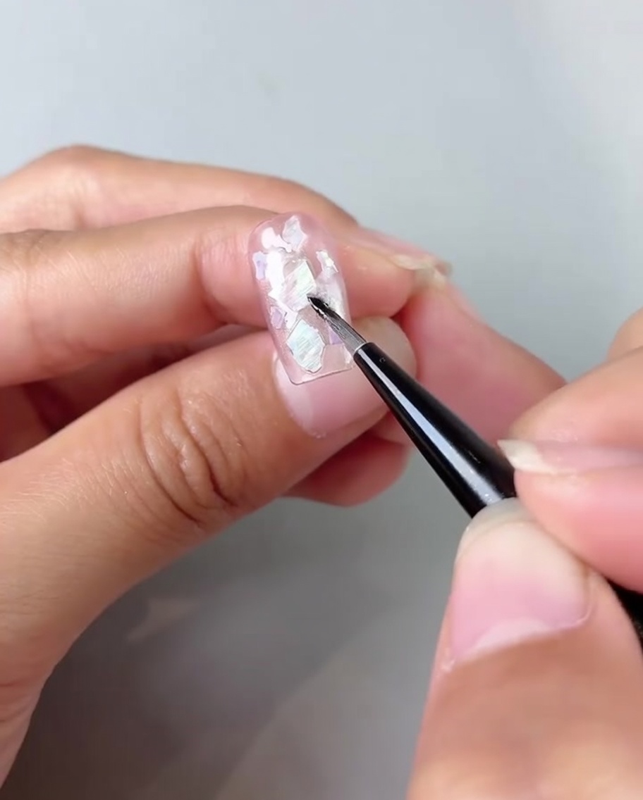 A brush blending milky white gel into the corners of a pink cat-eye nail.