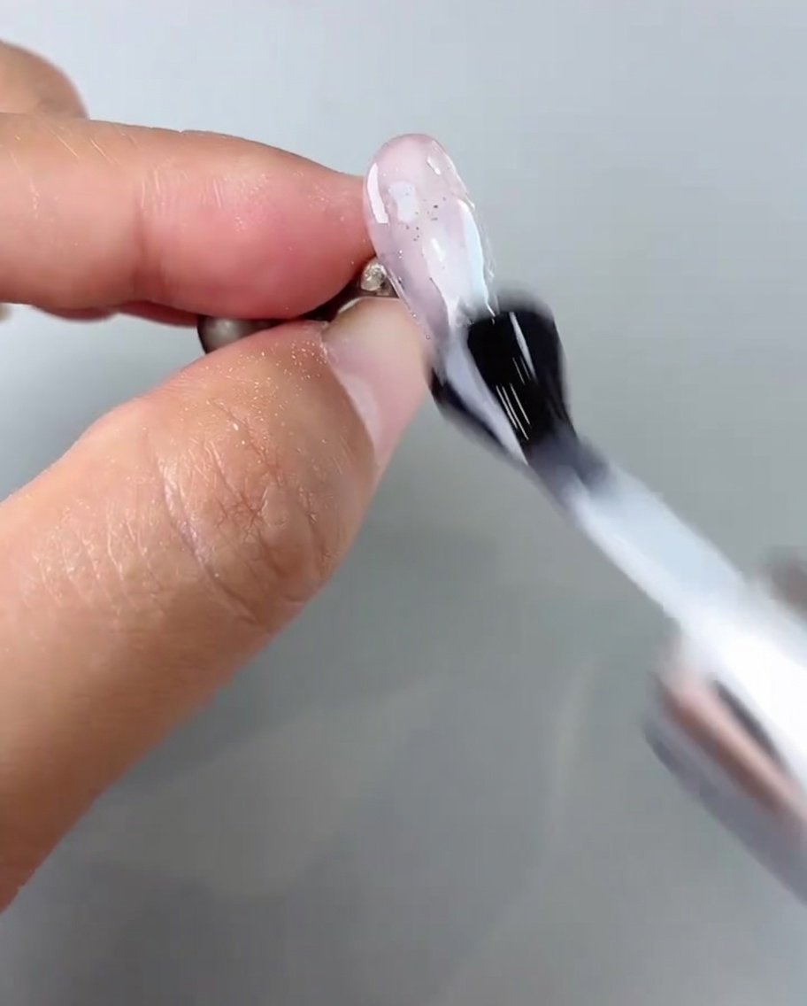 A brush applying a glossy top coat over the completed nail art.