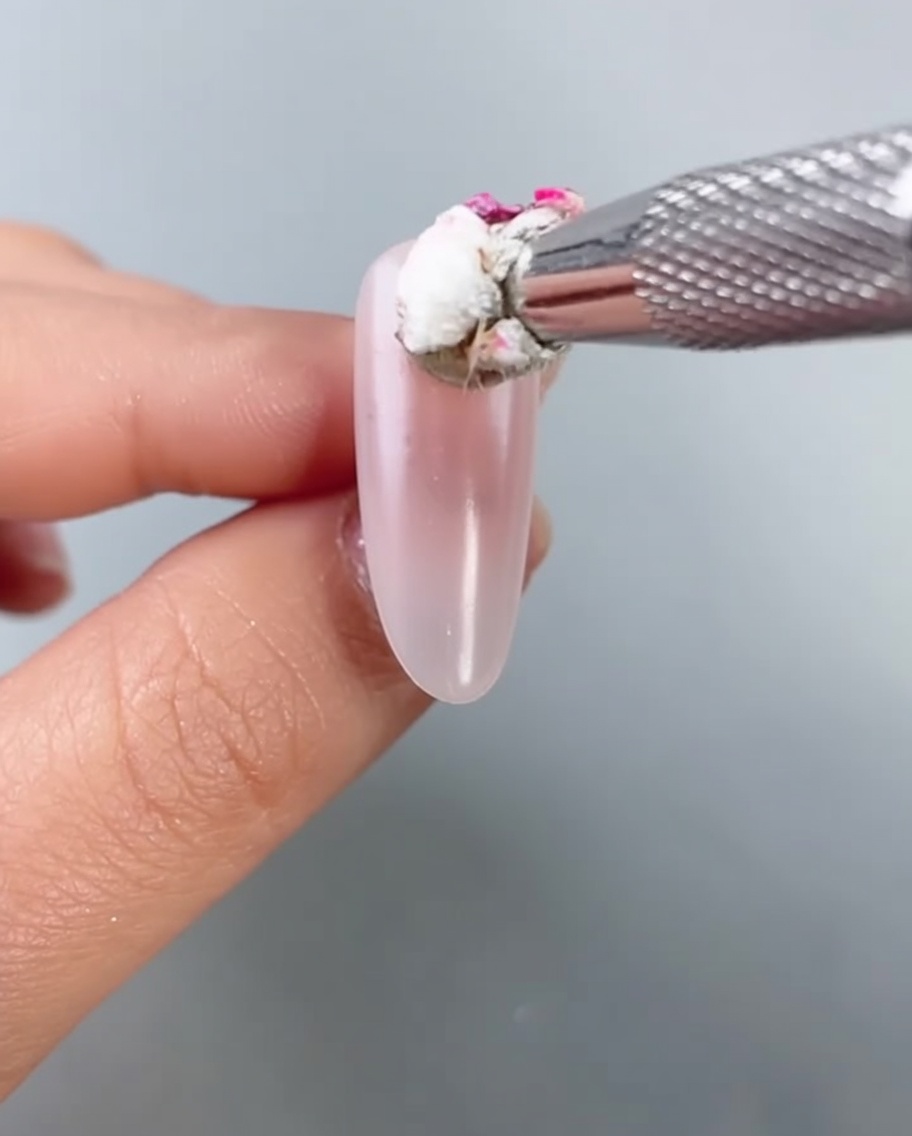 A close-up of a small sponge tool dabbing bright pink gel color onto the center of an almond-shaped nail to create a diffused blush effect.