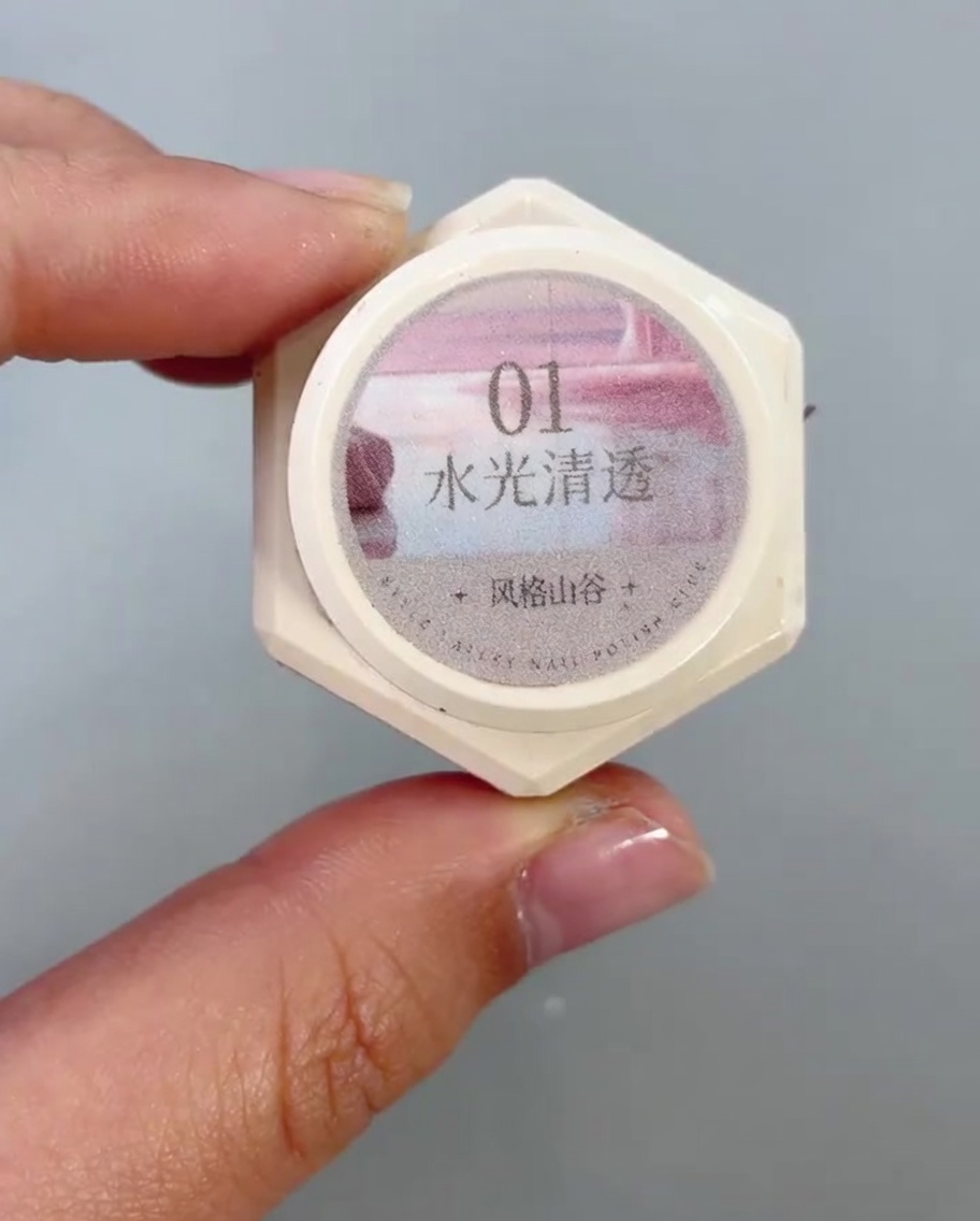 A nail brush applying a clear, shimmering cat-eye gel to the lower half of a nail.