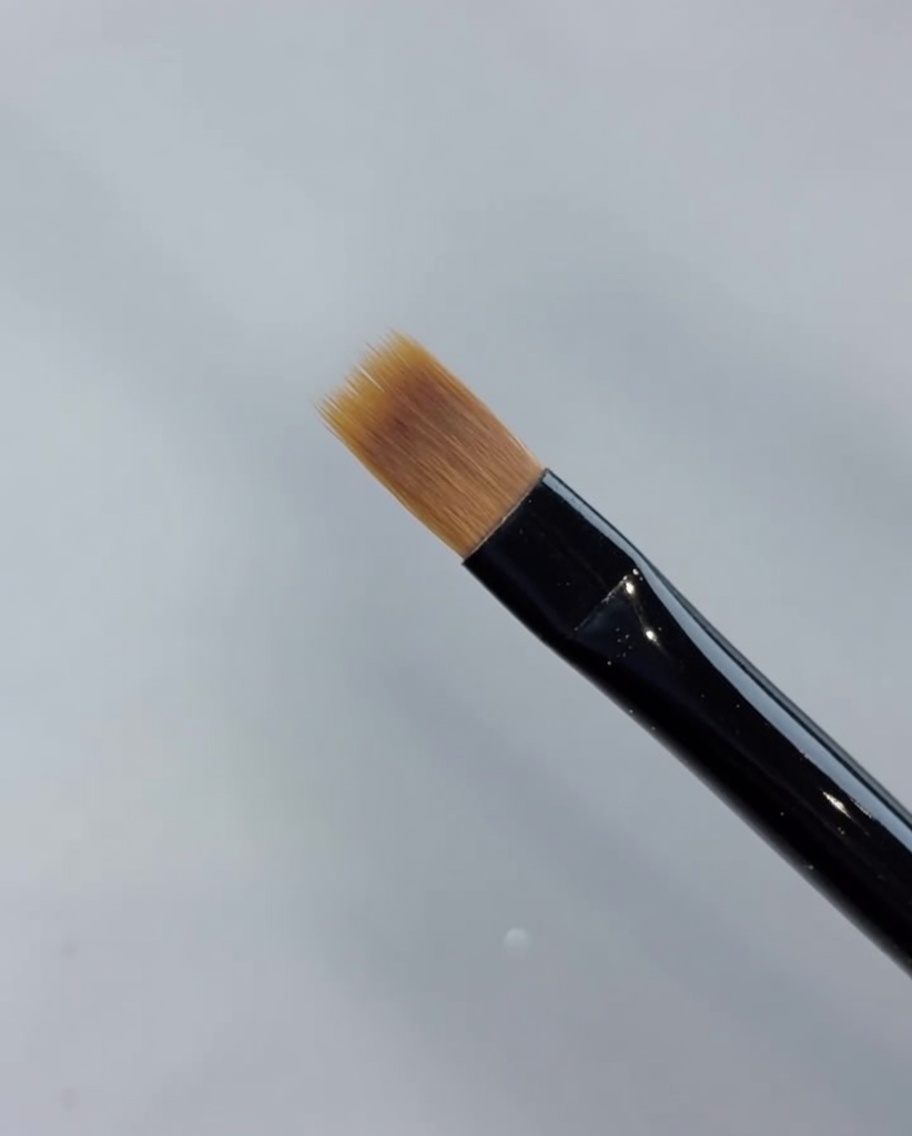 A close-up of a sweep brush pulling gel polish forward to blend and create a gradient.