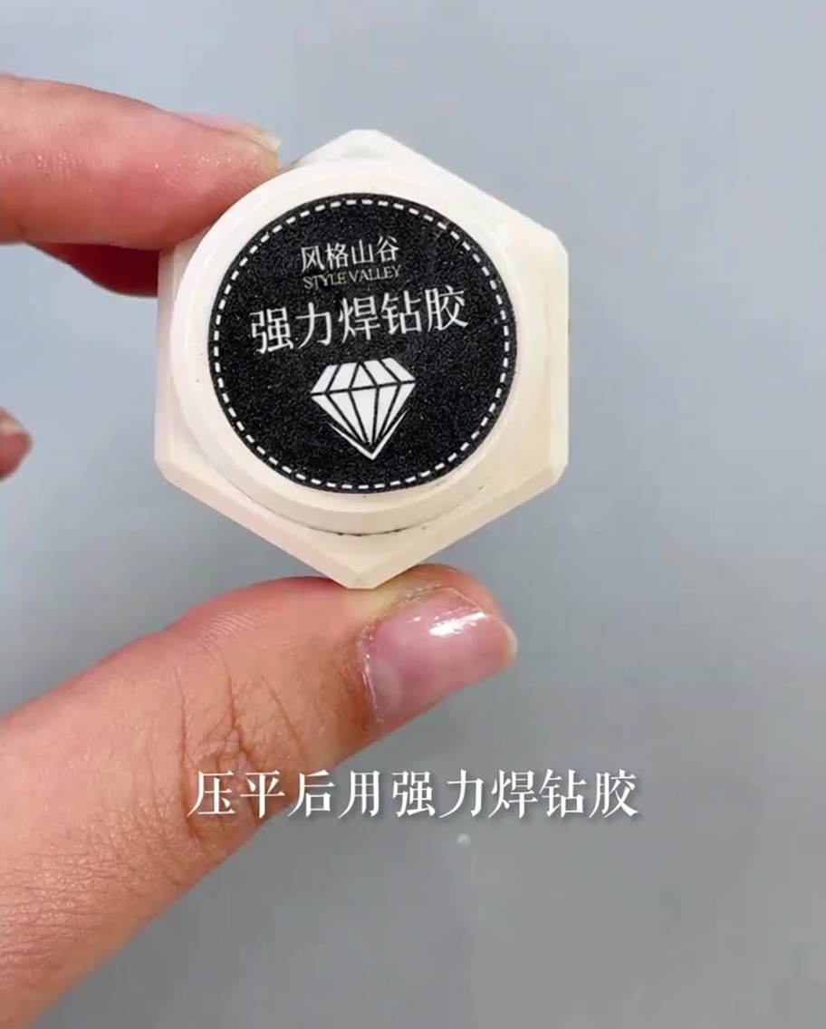 A small applicator brush applying a drop of clear, thick glue to the body and wings of a butterfly nail art piece.