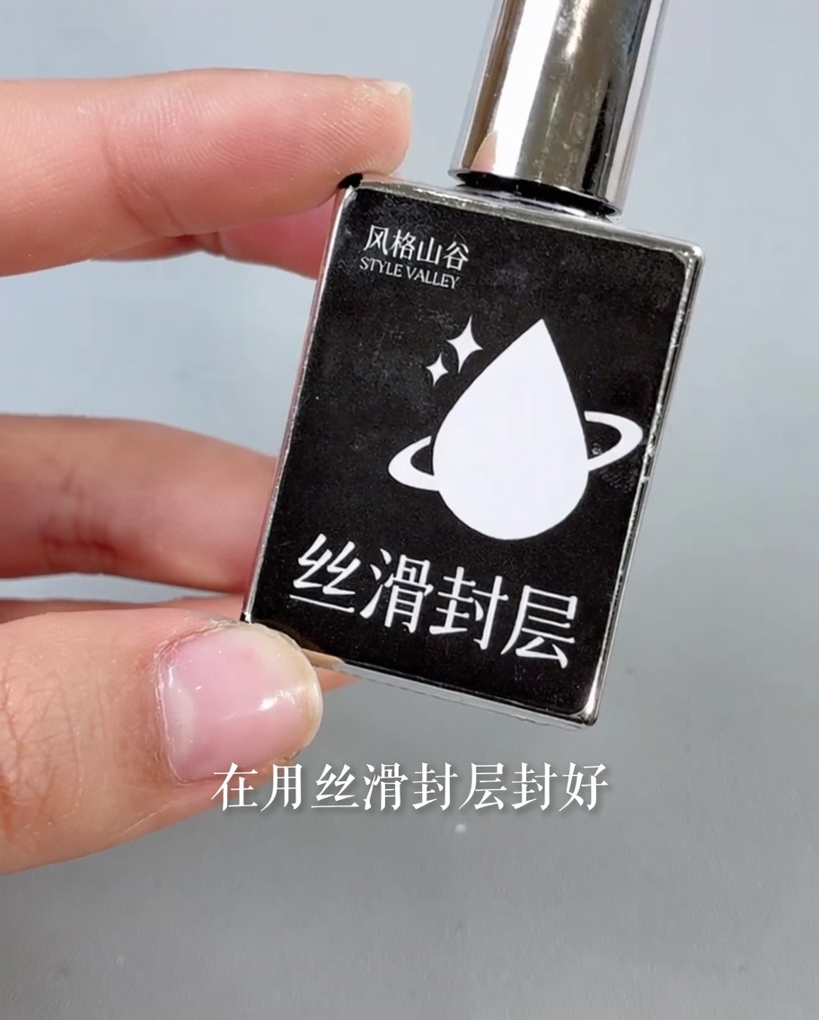 A brush applying a glossy clear top coat over a finished nail design.