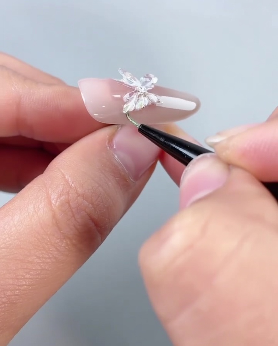 A brush applying clear filling glue along the bottom edge of a butterfly-decorated nail.