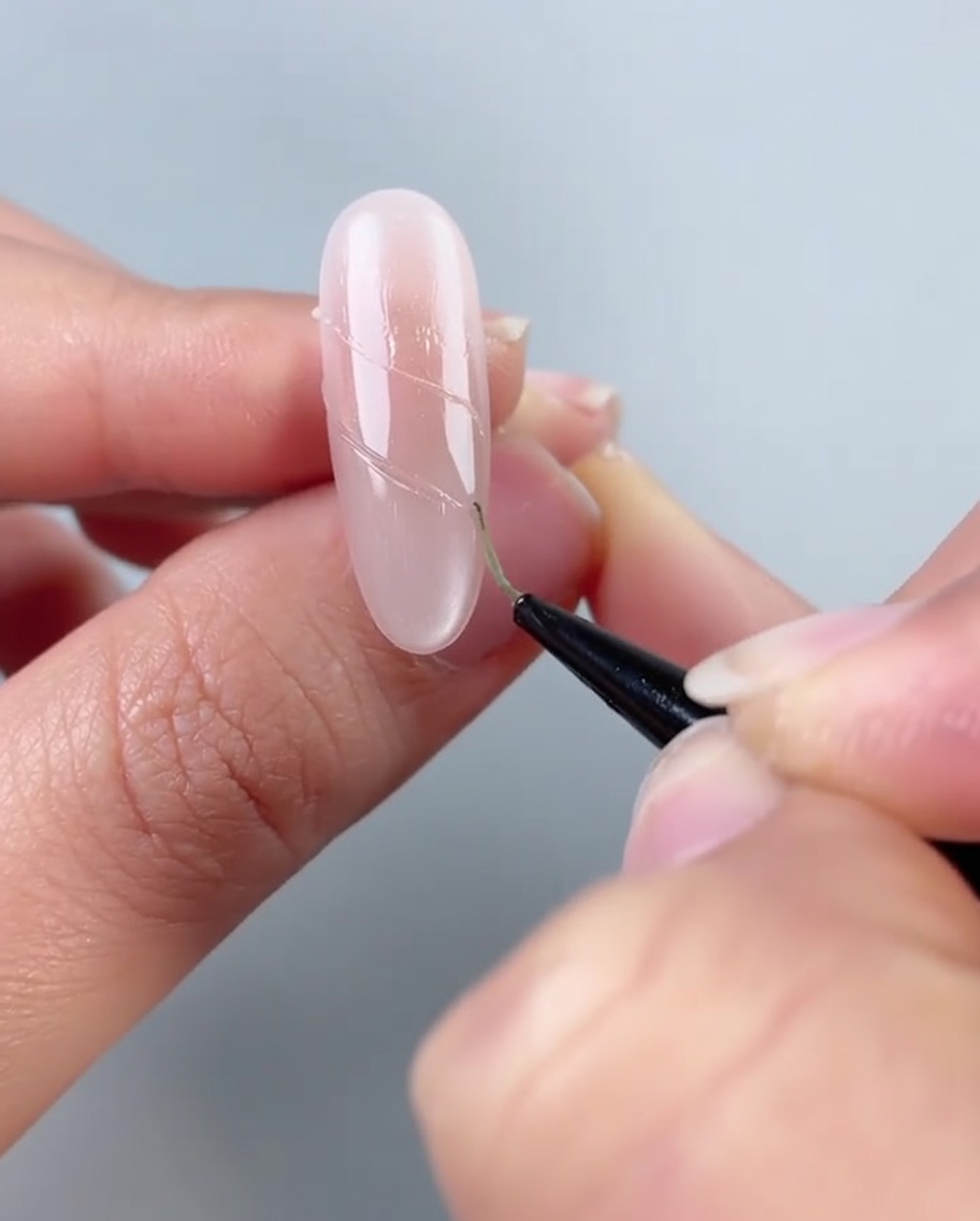 A nail showing a line of small white pearls and clear diamonds being placed onto adhesive glue lines.