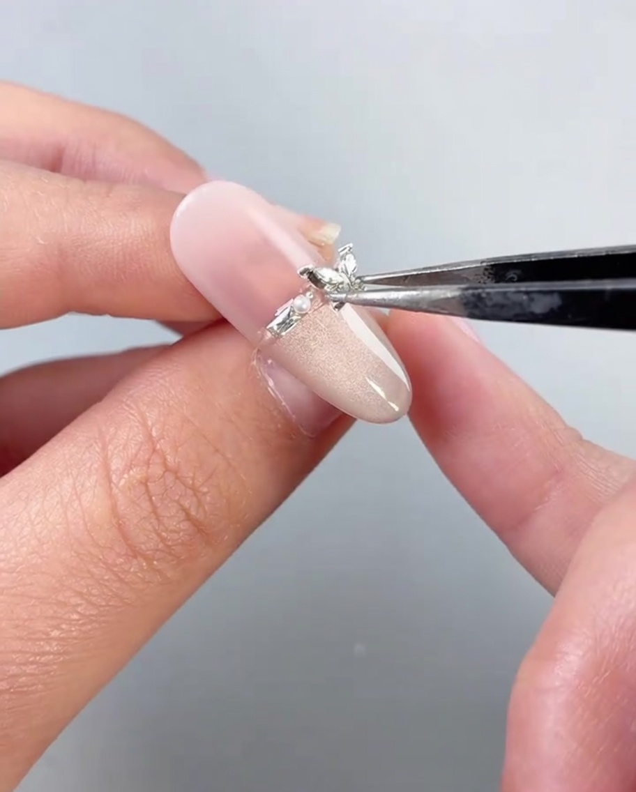 Tweezers placing a metallic butterfly charm onto a decorated fingernail.