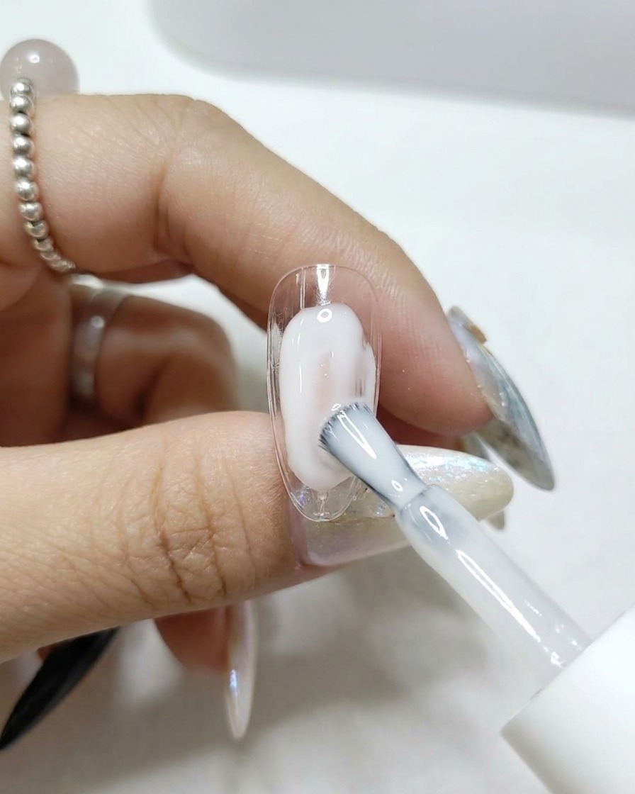 A brush applying a clear, glossy top coat onto a transparent nail tip.