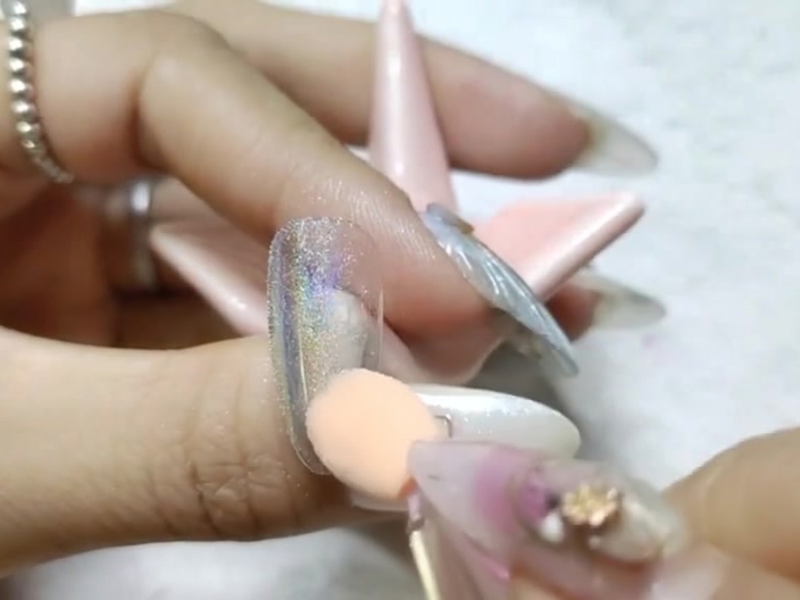 A sponge applicator rubbing chrome powder onto the nail surface to create a mirror-like finish.