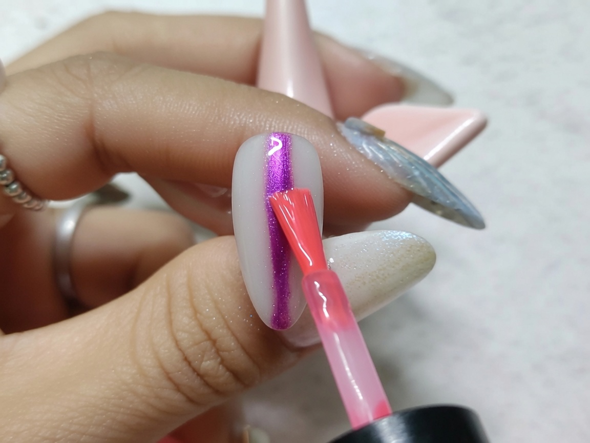 A nail art brush applying a bold, vertical stripe of bright red watercolor ink down the center of a metallic-finished nail.