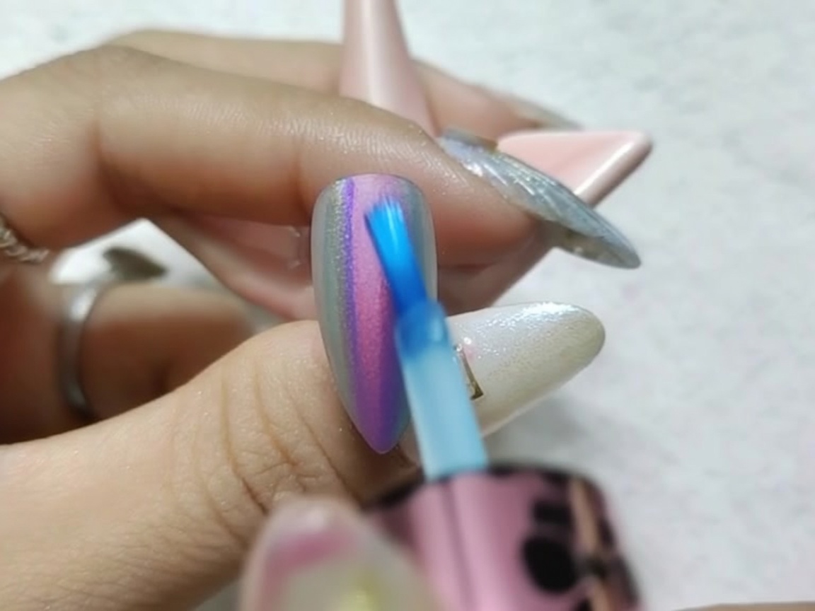 A close-up of a brush carefully blending the wet edges of red and blue watercolor ink on a chrome nail to create a smooth transition.