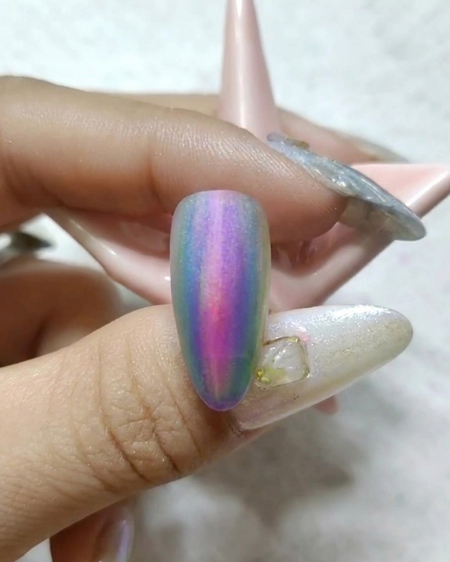 A brush painting a vibrant yellow stripe onto the side of a nail already featuring a red and blue watercolor gradient.
