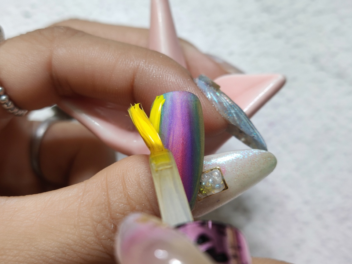 A brush applying a clear, glossy top coat over a finished colorful watercolor gradient nail design.