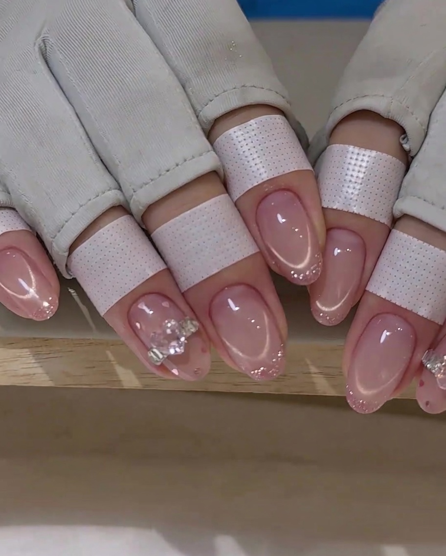 A thin brush creating a soft pink French tip line on a manicured nail.