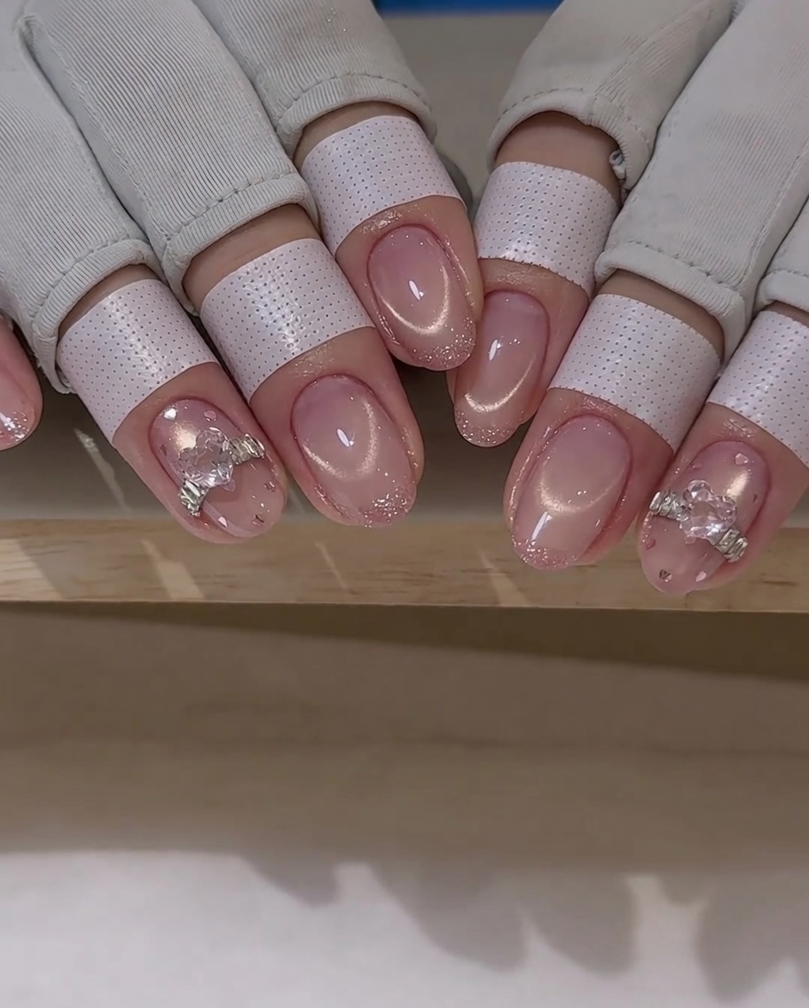 A nail art brush applying a thin layer of top coat around a crystal charm on a nail.