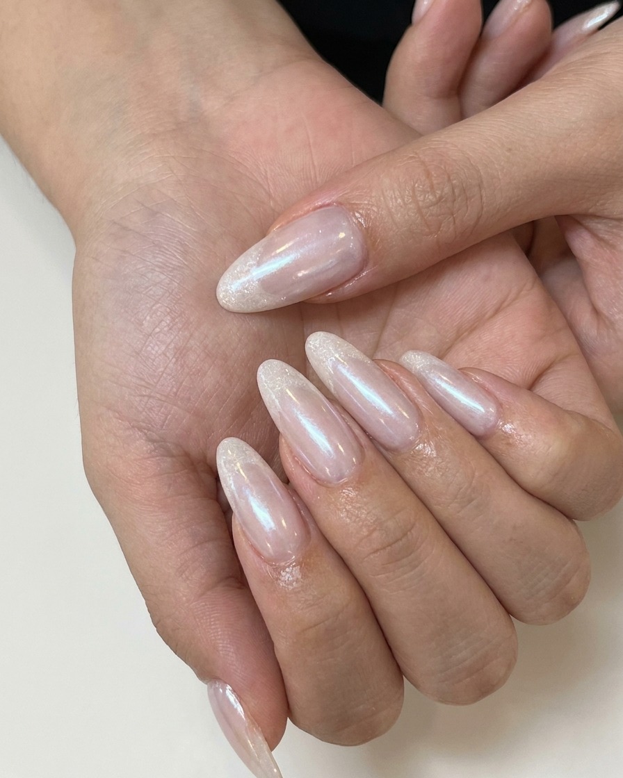A nail technician applying matte top coat over a nude pink gel nail.