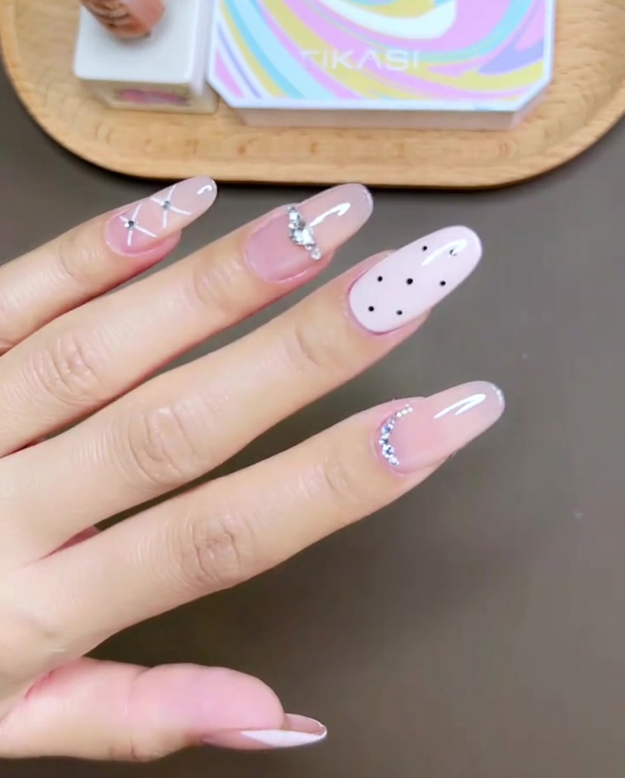 A close-up of a pink gel polish brush applying color to a middle finger nail.
