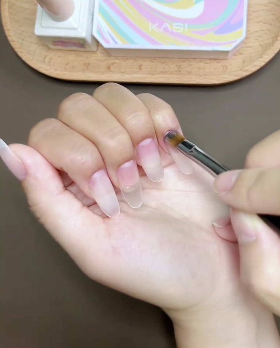 A brush applying clear reinforcement gel over a prepped nail surface, creating a smooth and leveled finish.