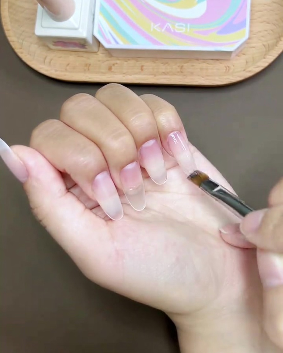A pair of tweezers placing a tiny crystal rhinestone on the surface of a thumb nail.