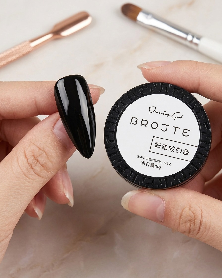 A hand holding a small black jar of white drawing gel, with nail art brushes visible in the blurred background.