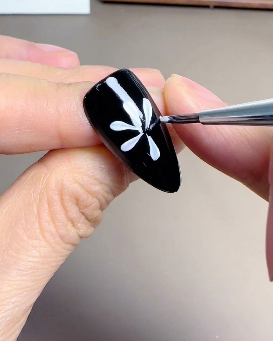 A top-down view showing a completed daisy flower design with white petals painted on a black nail.