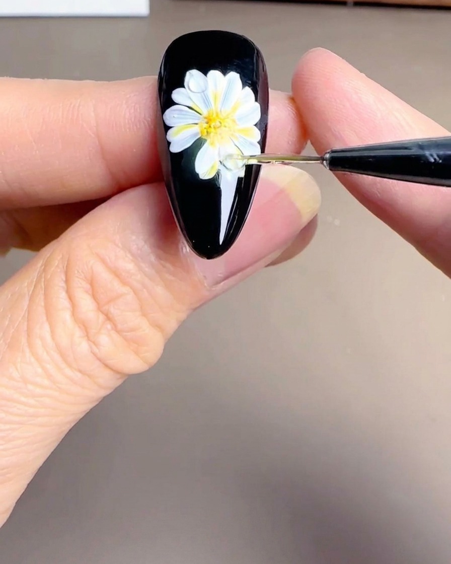 A close-up view of the center of a painted daisy on a nail, with tiny white dots adding detail to the yellow and orange core.