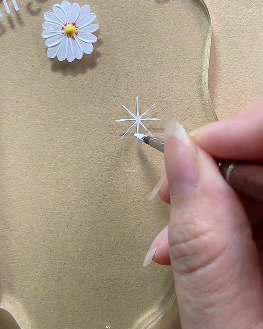 A close-up showing a brush adding white gel to thicken a diagonal line into a rounded teardrop petal.