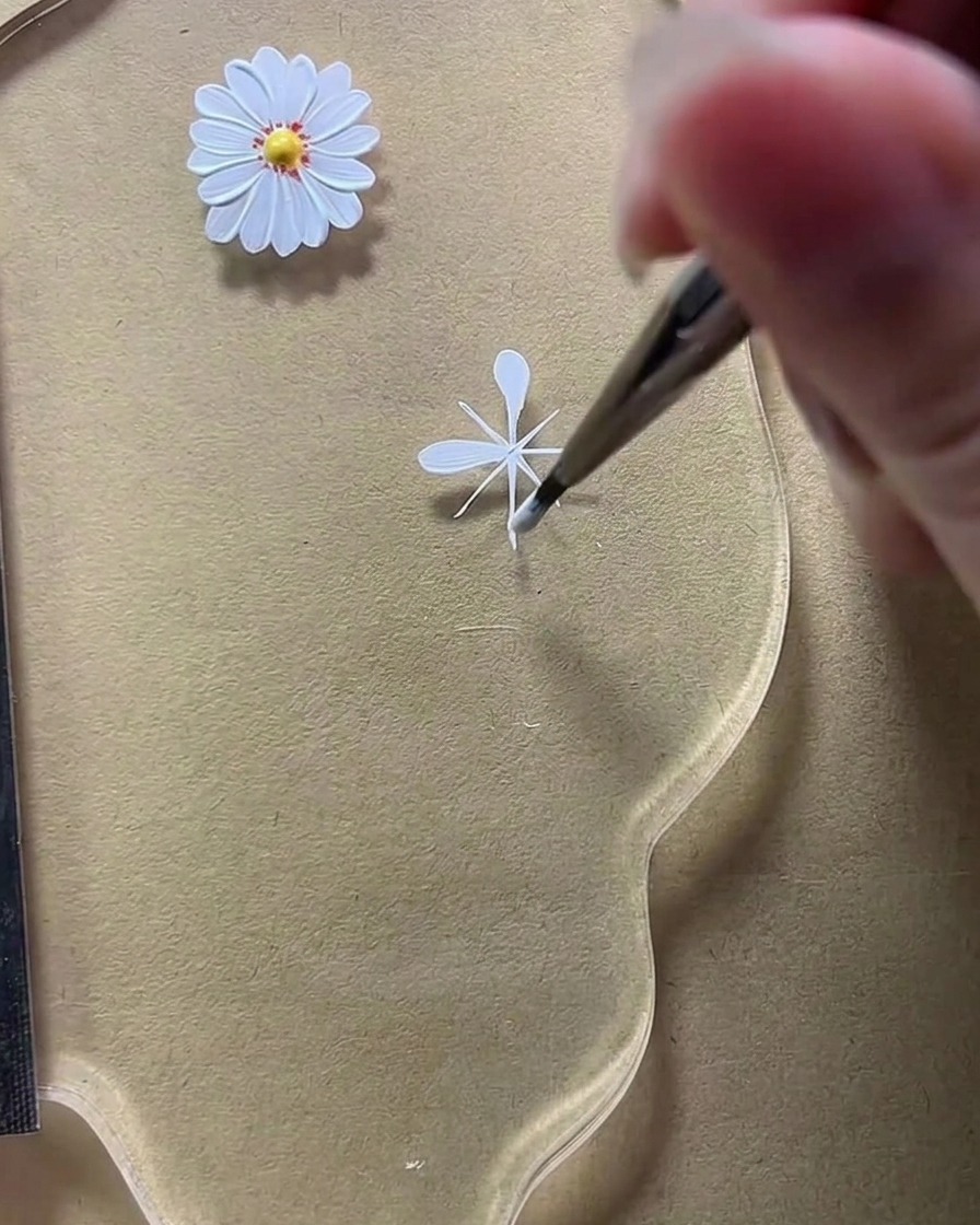 A close-up of a liner brush shaping a second rounded petal on the bottom-left diagonal guide line.