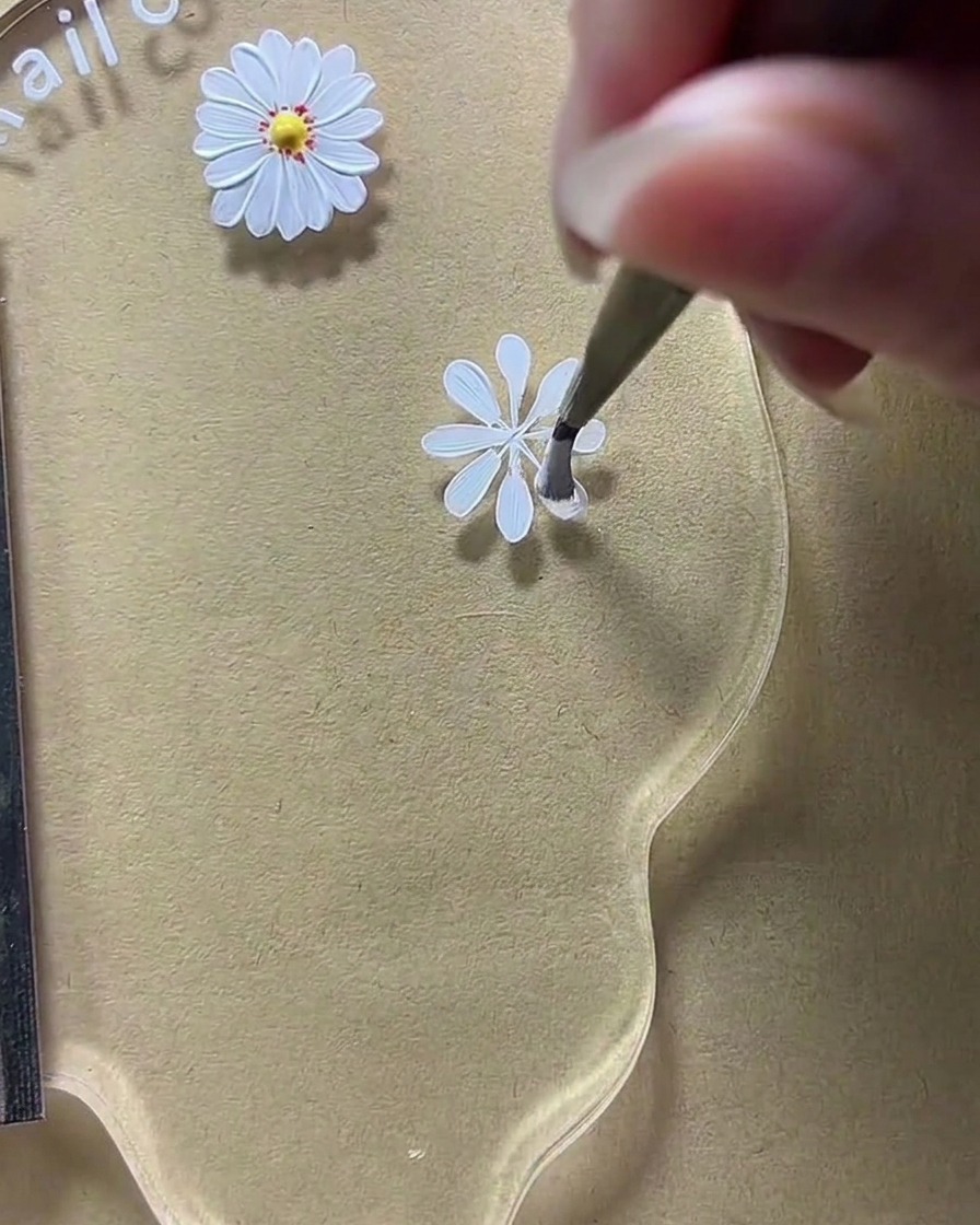 A close-up of a nail art palette where a brush is widening the white petal shapes on a daisy design.