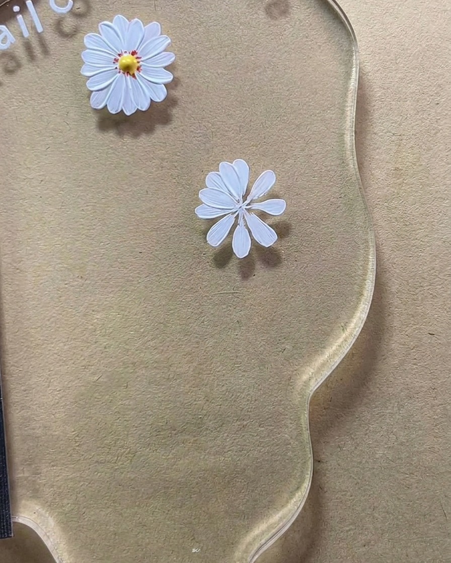 A close-up of an eight-petal white daisy design being completed on a nail art palette.