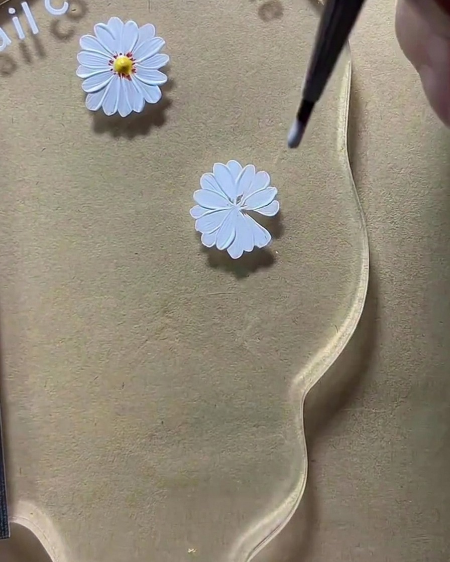A dotting tool placing a yellow center dot onto a white daisy petal design.