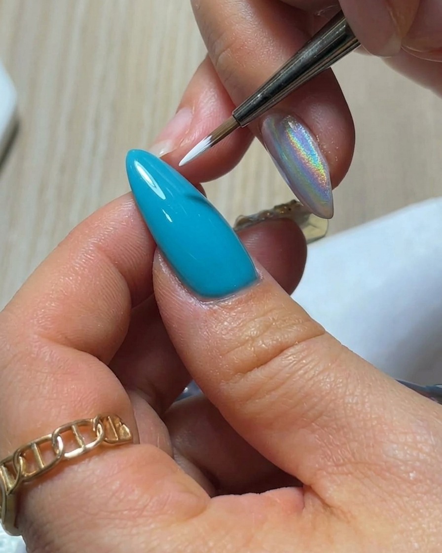 A close-up view of a fine liner brush applying a single, teardrop-shaped white gel petal onto a bright blue nail surface.