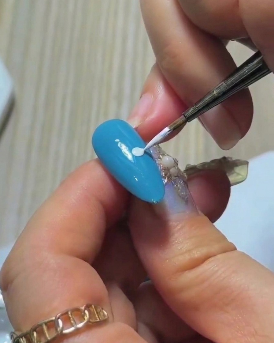 A close-up of a fine liner brush tip being dipped into a small amount of white gel polish on a palette.