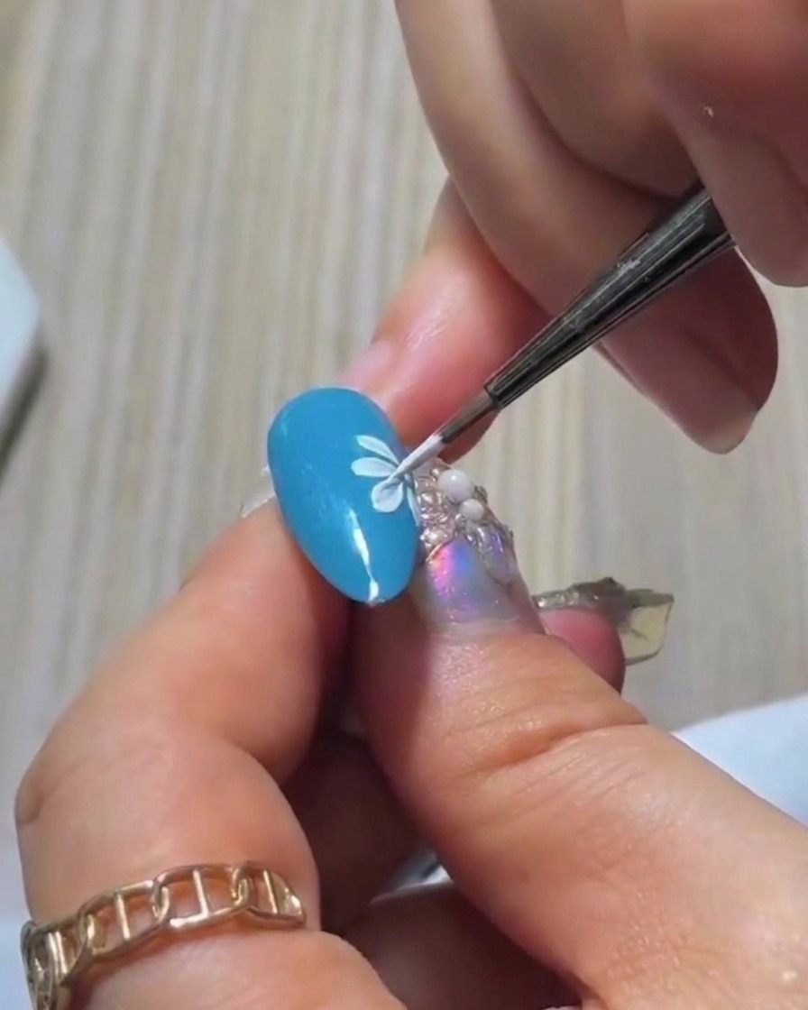 A close-up shot of the fourth white petal being painted on the blue nail, building the initial row of the daisy design.