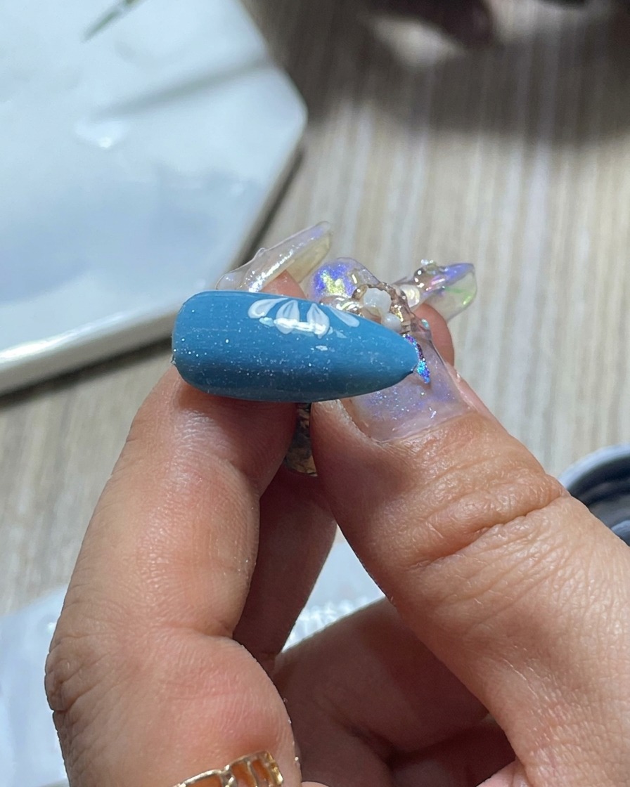 A close-up of a nail artists brush being wiped on a palette to control the amount of white gel polish.