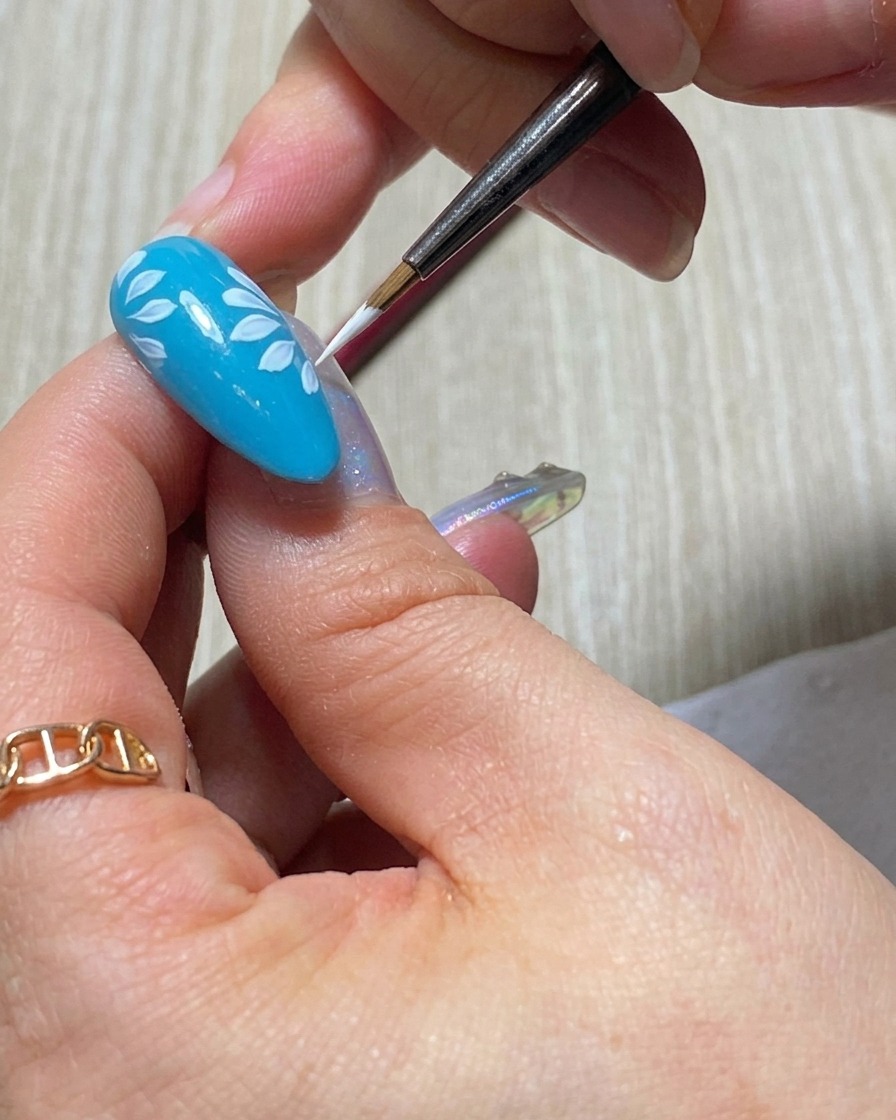 The tip of a liner brush applying a bold, opaque white petal for the second layer of a daisy design.