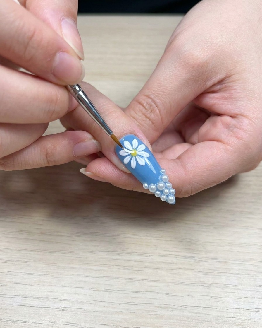 Close-up view of a brush applying white gel to a daisy petal to improve color density.