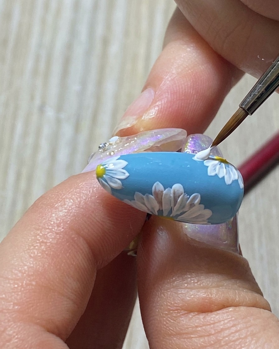 A fine brush stippling tiny white dots into the center of a painted daisy.