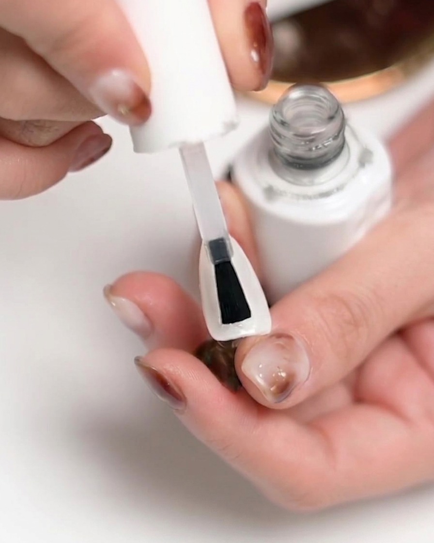 A hand positioned inside a UV/LED nail lamp with light shining, indicating the curing process.