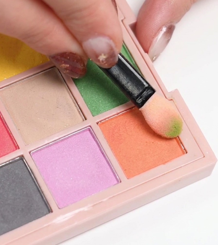 A makeup sponge picking up orange gel polish from a palette to apply to a nail.