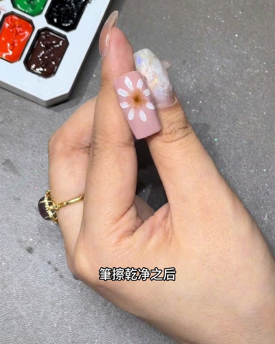 A close-up view of a brush blending white flower petals on a pink nail base to create a soft, gradient effect.