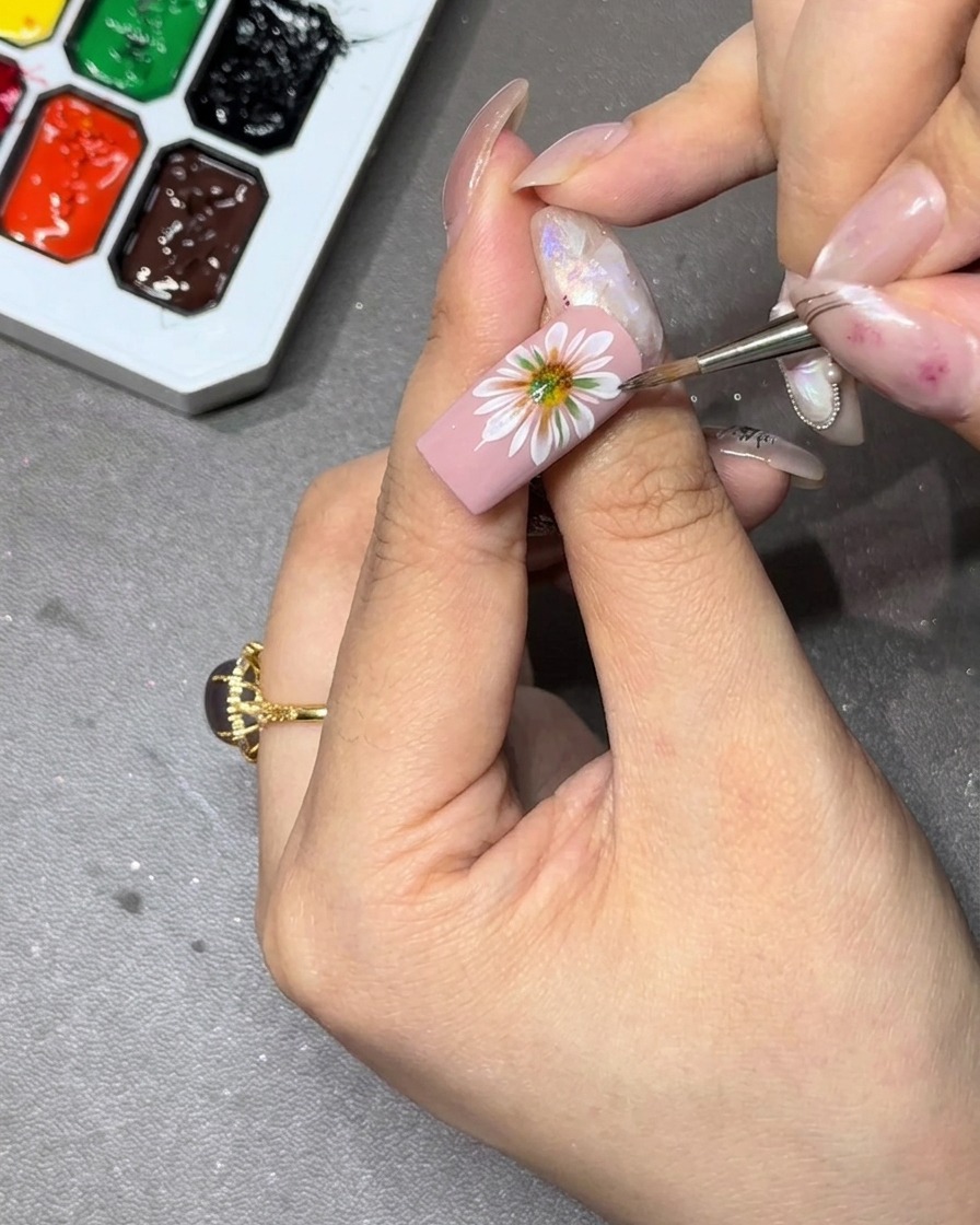 A brush tip carefully feathering out the inner edges of a white flower petal to perfect the gradient on the nail.