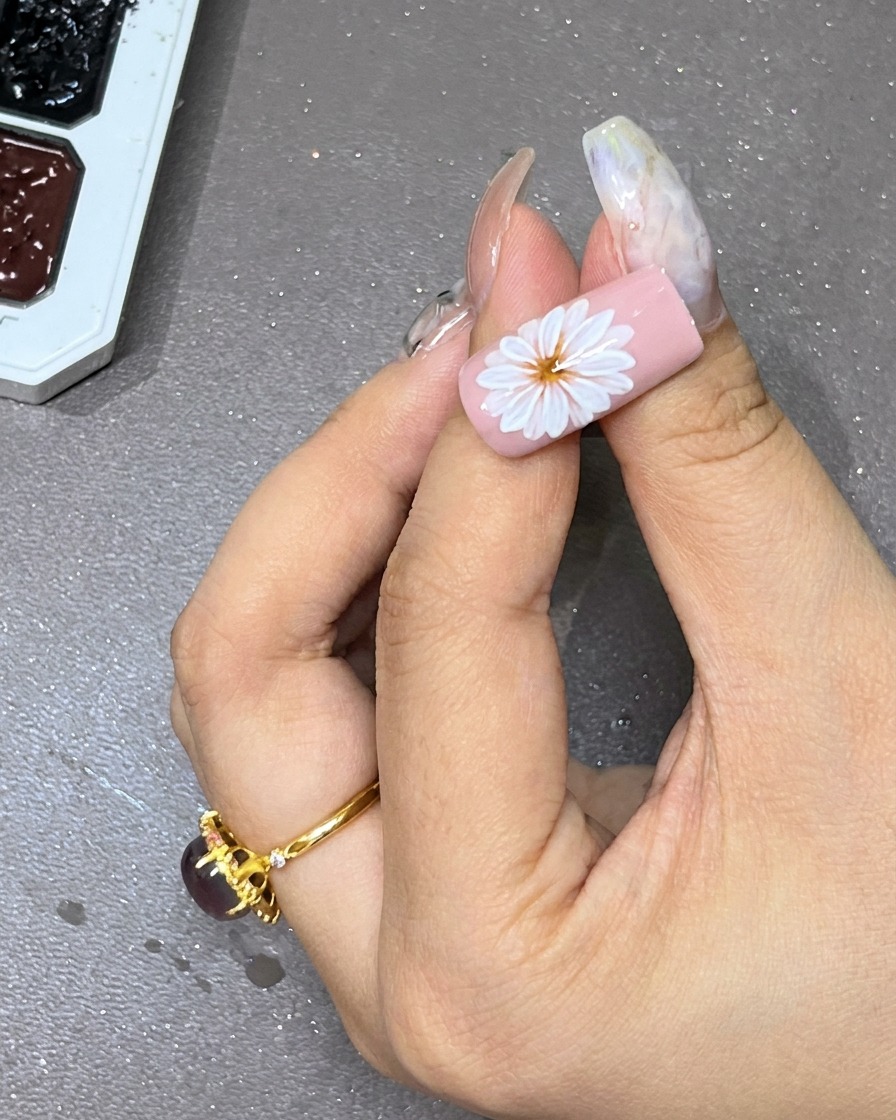 A dot of black gel being carefully placed in the center of the white layered flower on the nail.