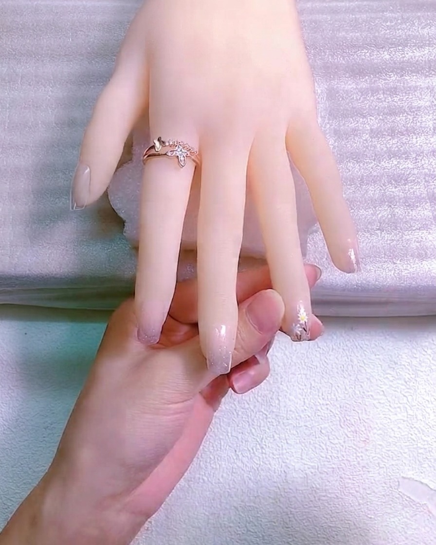 A close-up of a dotting tool applying a yellow gel center to a small hand-painted white daisy on a fingernail.