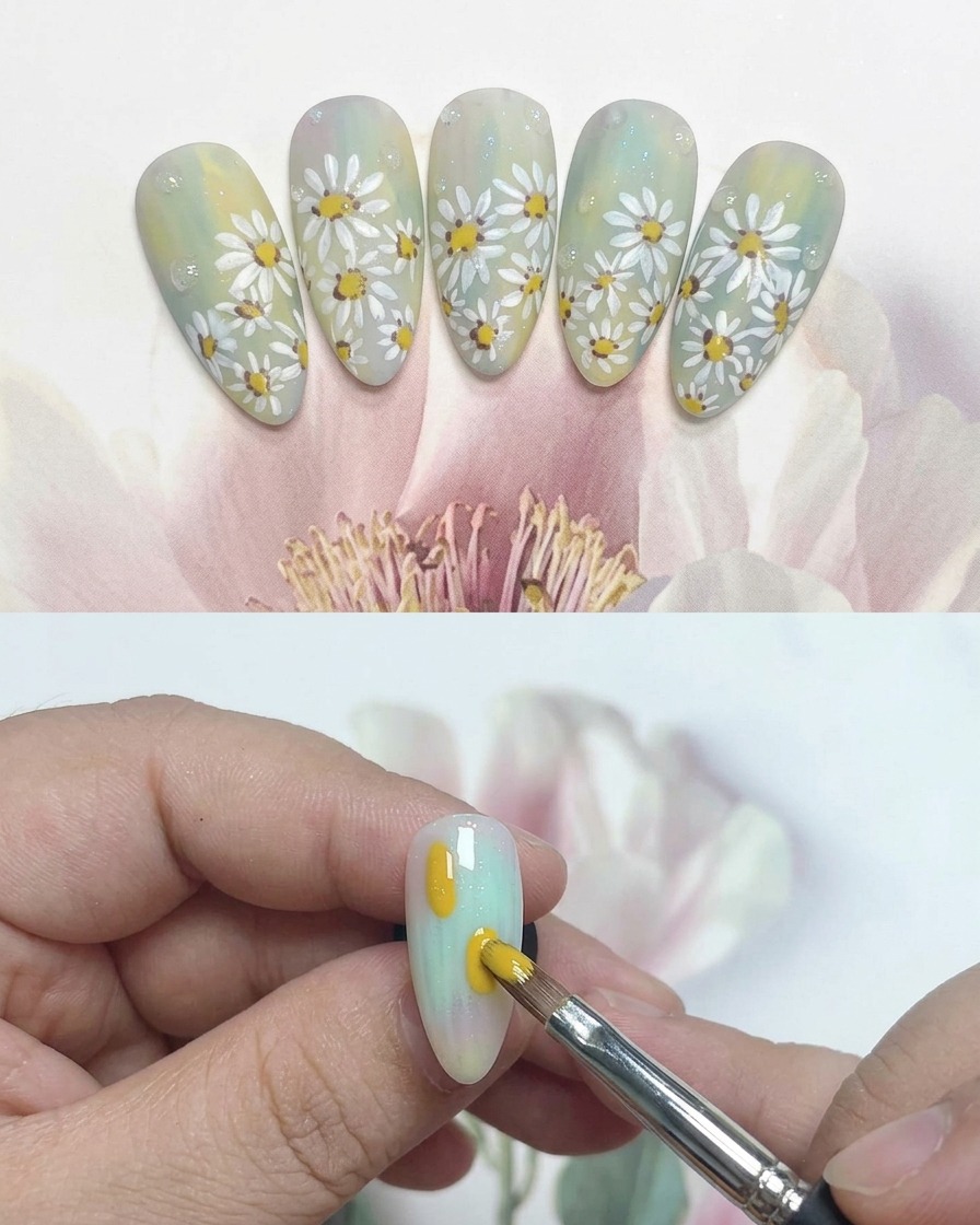 A fine liner brush creating white petals around a yellow center on a nail.